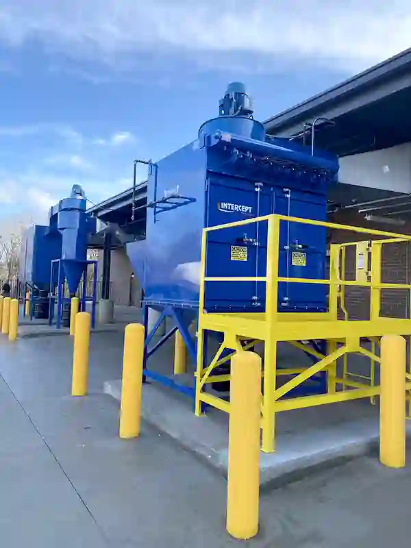 Large outdoor ProVent Intercept industrial dust collection units with yellow service platforms, safety railings, and connected ductwork, installed for efficient dust and particle filtration at an industrial facility.