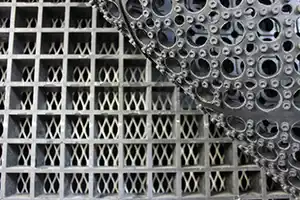 Close-up of grated industrial work surface with layered metal grid and perforated structure, providing durability and stability for industrial applications.