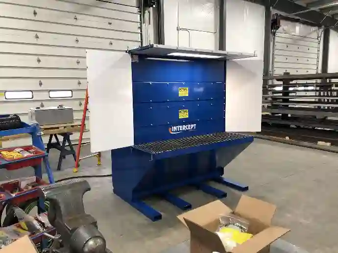 Intercept industrial dust collection unit in a workshop setting, featuring a grated work surface, side panels, and caution labels, designed for air filtration and dust management.