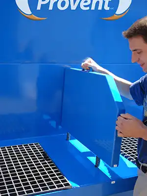 Person installing a center partition on a ProVent industrial dust collector, with a grated work surface and blue machine casing for optimized dust collection efficiency.