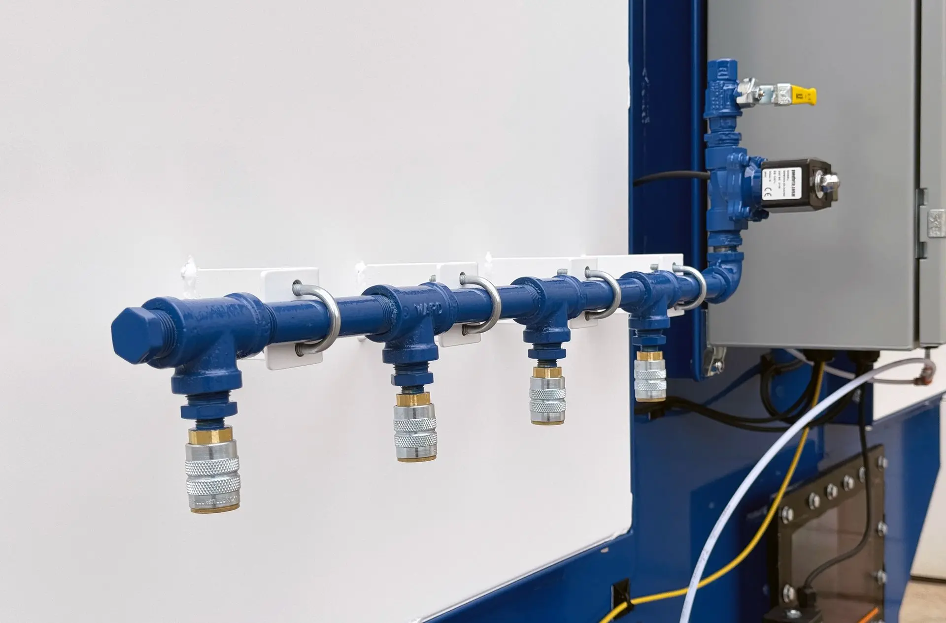 A compressed air manifold with four quick-connect couplers mounted on a panel. Connected to a solenoid valve and control box, this setup provides centralized air distribution for industrial systems.